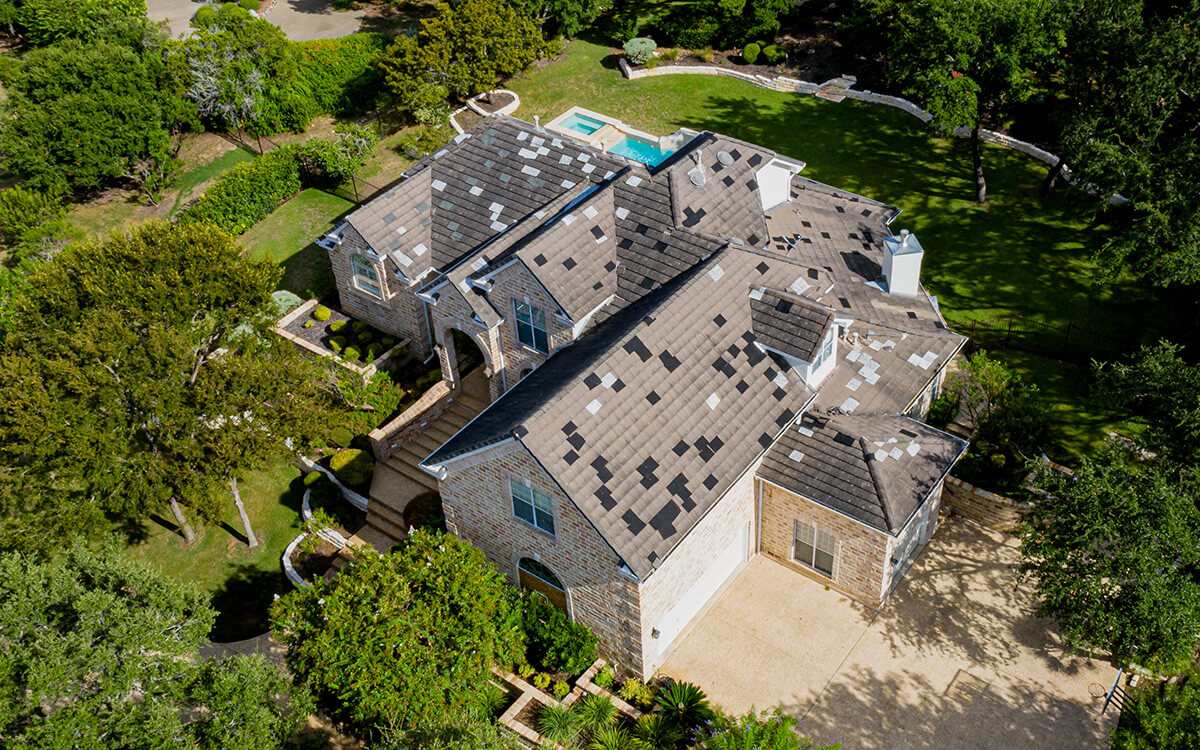 Aerial drone view of a residential roof in San Antonio, Texas scattered with hail-damaged shingles after a severe hailstorm